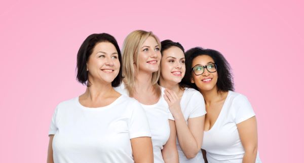 Grupo de mulheres diferentes e felizes, vestindo camisetas brancas sobre fundo rosa.