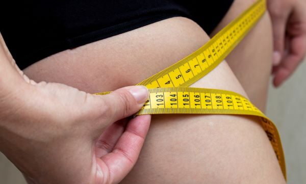 Mulher que mede a coxa com a fita métrica amarela.