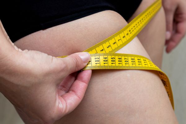 Mulher que mede a coxa com a fita métrica amarela.