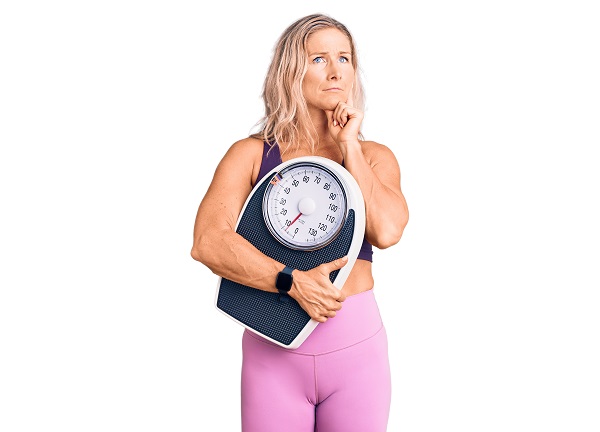 Mulher loira de meia idade, com expressão de dúvida, segura uma balança com o braço direito. 
Durante a menopausa podem ocorrer alterações significativas no metabolismo da mulher.